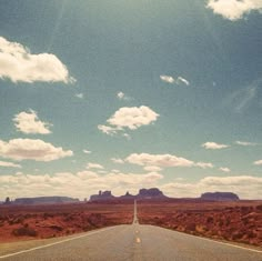 an empty road in the middle of nowhere with mountains in the distance and clouds in the sky