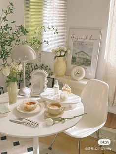 a white table topped with plates and bowls filled with food next to flowers in vases