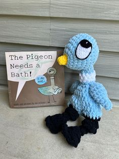 a crocheted blue bird next to a book about the pigeon needs a bath