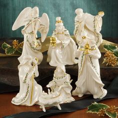 three white angel figurines with gold accents on a table next to holly leaves