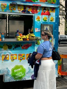 a woman standing in front of a food truck with fruit on the side and she's wearing a blue shirt