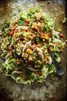 a salad with chicken, lettuce and tomatoes on a metal tray next to a fork