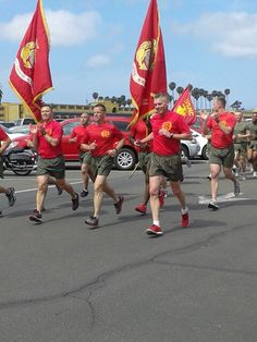 men in red shirts and green shorts are running down the street with flags on their backs