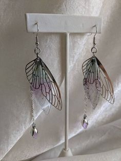 These gorgeous and delicate fairy earrings feature metal and resin wings with a hanging drop crystal. Perfect for special occasions or to add a bit of magic to your every day! The primary color refers to the metal The secondary color refers to the resin wing Silver Fairycore Earrings For Party, Silver Fairy Grunge Dangle Jewelry, Fairy Grunge Silver Dangle Jewelry, Silver Fairy Earrings For Party, Silver Fairy Style Party Earrings, Fairycore Silver Earrings For Gift, Silver Fairy Grunge Earrings For Gift, Fairy Grunge Silver Earrings For Gift, Fairy Style Silver Earrings