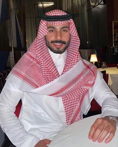 a man sitting at a table wearing a red and white scarf over his head with a smile on his face