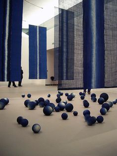 some balls are in the middle of a room with blue curtains and people walking by