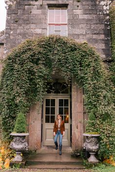 a woman standing in front of an old building with ivy growing on it's walls