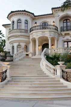 a large white mansion with stairs leading up to it's front door and balconies