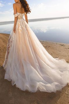 a woman in a wedding dress standing on the beach looking off into the distance with her back to the camera