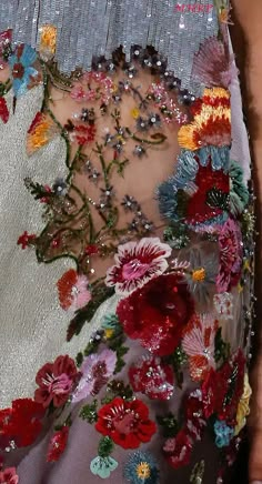 a woman's hand holding onto a piece of fabric with flowers and beads on it