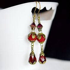 These handmade Siam Red Crystal Earrings combined opaque faceted rondelle and teardrop crystals.   Beautiful vintage style antique brass leaf petal bead caps and beads adorn these stunning red earrings. Juicy berry red Victorian Earrings are also set with clear crystal rhinestone pave beads, and topped with pretty ruby bicone crystals.   These boho long long red teardrop earrings have briolette drop adorned in antique gold brass have an elegant and romantic appeal.   They are so special, wear they from day into evening with ease.  Downton Abbey inspired artisan handcrafted by me, Ms.B.   These lovely siam red crystal earrings are beautiful in person.  Great gift for her! *♥  ♥* ♛ Earrings Length ~ 2 1/2" inches long ❥ M a t e r i a l s  ↬ Rondelle Crystals 10mm ↬ Teardrop Crystals 12x8mm ↬ Birthday Things, Crystals Beautiful, Victorian Earrings, Artisan Jewelry Handmade, Red Jewel, Pave Beads, Jeweled Earrings, Earring Ideas, Long Dangle Earrings