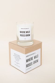 a glass candle sitting on top of a cardboard box that says where wild roses grow