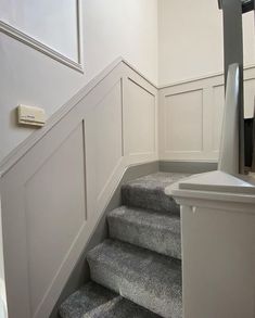 there is a staircase leading up to the first floor in this house with white paneling and gray carpet