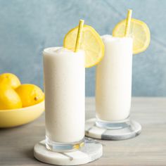 two glasses filled with lemonade sitting on top of a table next to some lemons