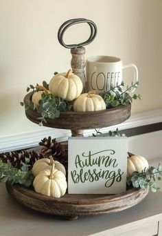 two tiered trays holding pumpkins and greenery with coffee mug on top