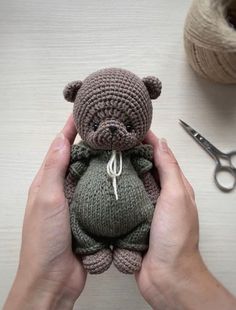 a person holding a small teddy bear in their hands next to some yarn and scissors