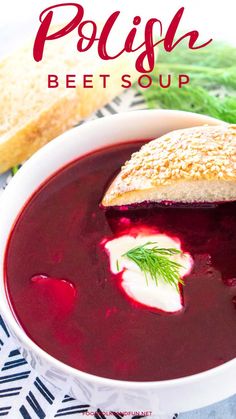 a white bowl filled with beet soup next to bread and green leafy garnish