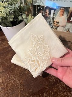 a hand is holding a white handkerchief on a table next to a potted plant