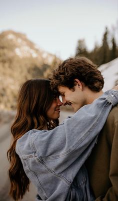 a man and woman embracing each other on the side of a road with mountains in the background