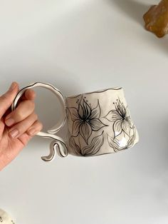 a hand holding a coffee cup with flowers painted on the outside and inside, in front of a white background