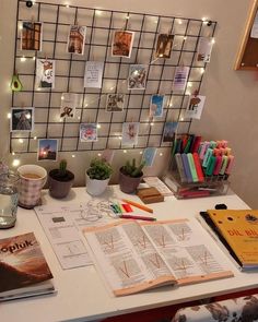 a desk with books, pens and pictures on the wall behind it is lit up by fairy lights