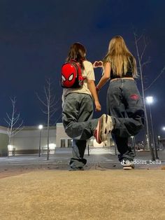 two people are walking down the street at night with backpacks on their backs and one is holding his hand