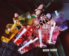 a person holding many different colored drinks in their hands with the caption moon tabbie