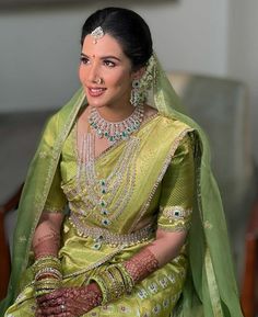 a woman in a green and gold bridal outfit sitting on a couch wearing jewelry