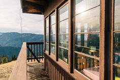 a wooden porch on the side of a mountain with mountains in the background and sun shining through windows