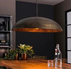 a large metal light hanging from a ceiling in a dining room with potted plants on the table