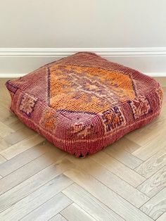 an orange and blue rug sitting on top of a wooden floor next to a white wall