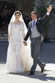 a bride and groom walking down the street holding hands in front of an audience at their wedding