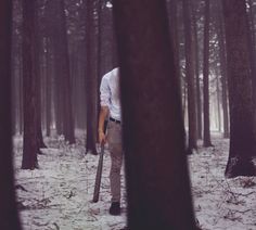 a man is walking through the woods with a long stick in his hand and wearing a white shirt