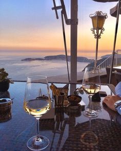 two glasses of wine sitting on top of a table next to an ocean view at sunset