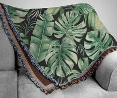 a green and black tropical leaf print throw blanket on a grey couch with fringe trim