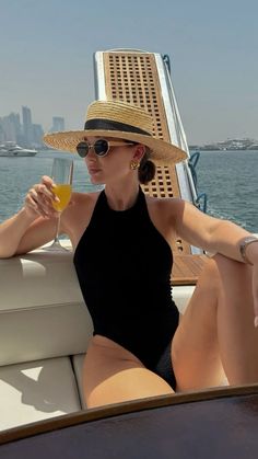 a woman in a hat and sunglasses sitting on a boat with a glass of wine