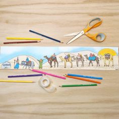 pencils, markers and scissors are sitting on a table next to an image of people riding camels