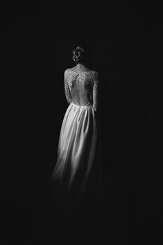 a woman in a long white dress standing in the dark with her back turned to the camera