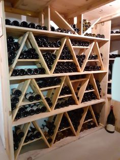 a wooden wine rack filled with lots of bottles next to a wall full of shelves