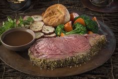 a plate with meat, potatoes and broccoli next to a bowl of dipping sauce