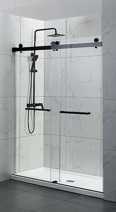 a walk in shower sitting next to a white tiled wall and black tile flooring