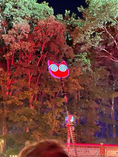 a red and blue owl shaped kite flying in the air above trees at night time