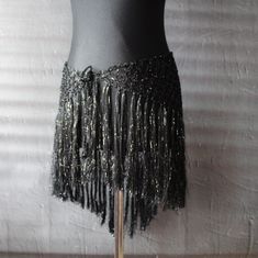 a mannequin is adorned with black sequins and gold beads on a wooden stand