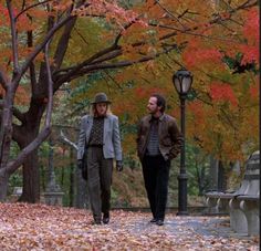 two people are walking through the park in autumn