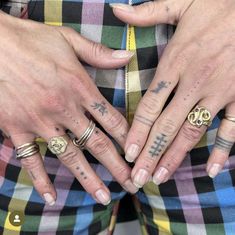 two people with tattoos on their hands and fingers, both wearing matching rings in different colors