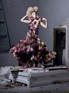 a woman in a dress made out of flowers is standing on top of a box