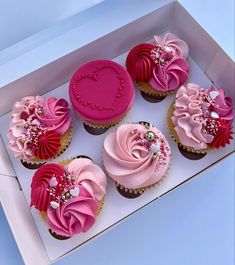 six cupcakes with pink frosting and heart decorations in a white cardboard box