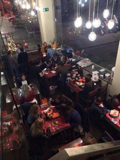 people sitting at tables in a restaurant with lights hanging from the ceiling and windows above them