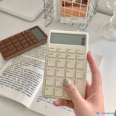 a person is holding a calculator in front of an open book on a table