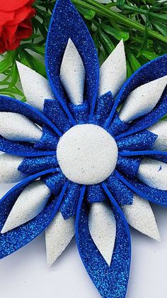 a blue and white flower with some red flowers in the background on top of a table